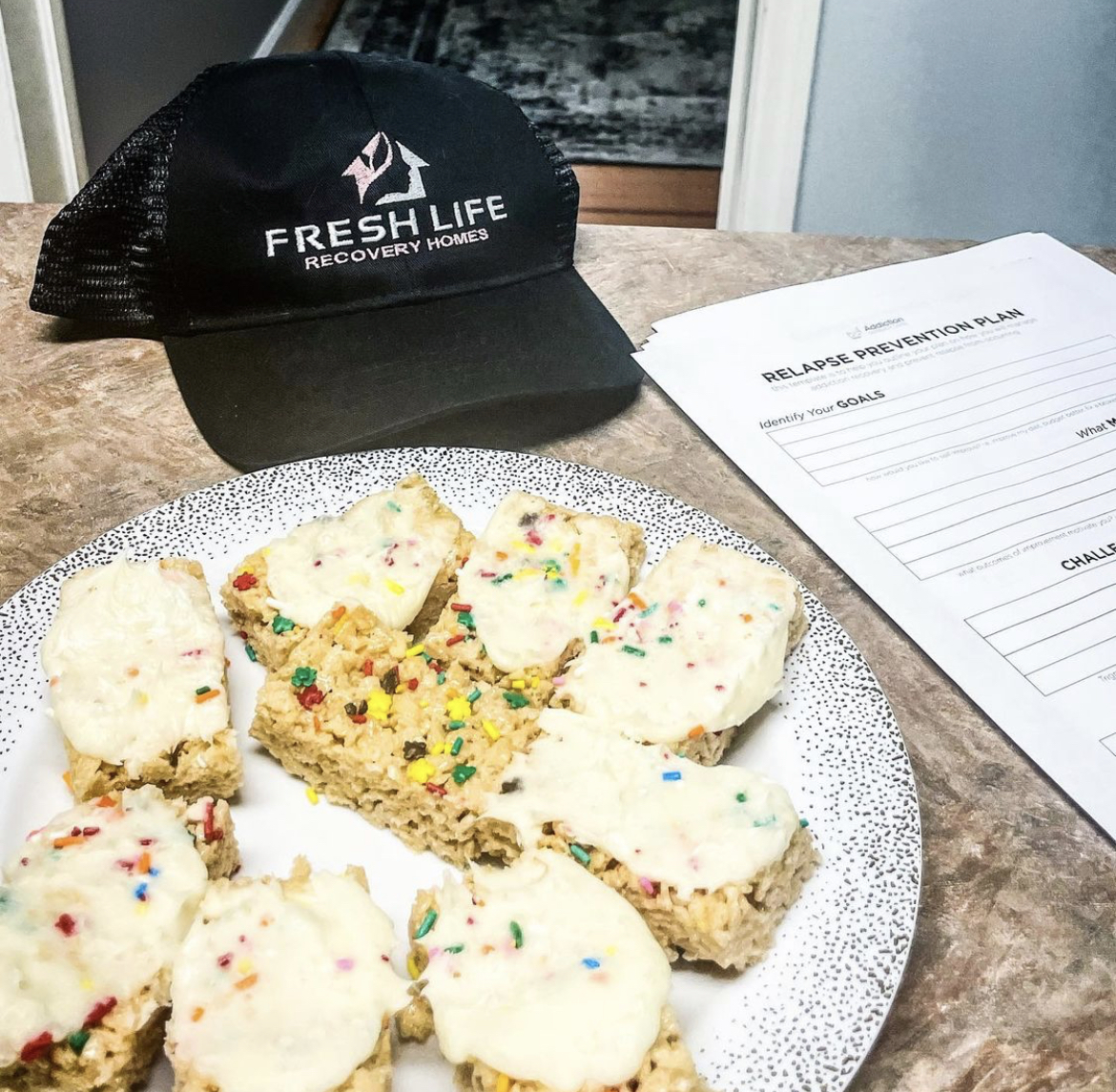 Plate up cake, a Fresh Life Recovery Homes baseball cap, and a Relapse Prevention Plan form on a table at Fresh Life Recovery Homes in Bradenton, Florida